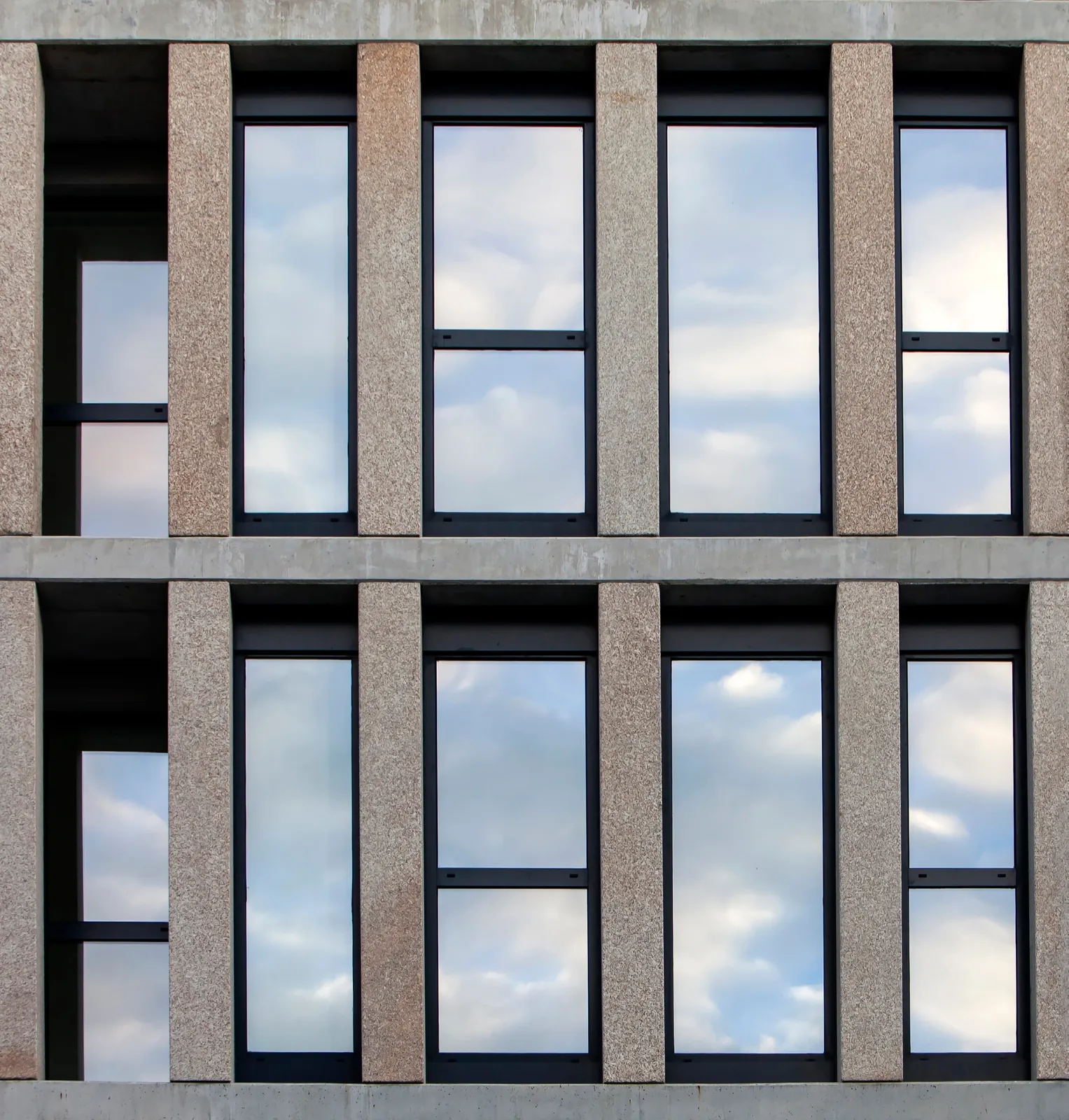 Building facade with two rows of black aluminium windows between stone pilasters