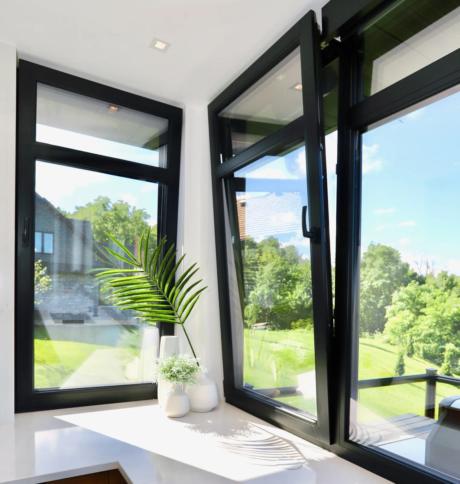 Black windows with one tilt-and-turn sash open onto a garden